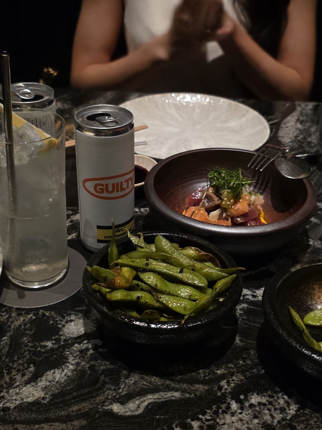 A Guilty can on a dinner table with edamame and raw fish