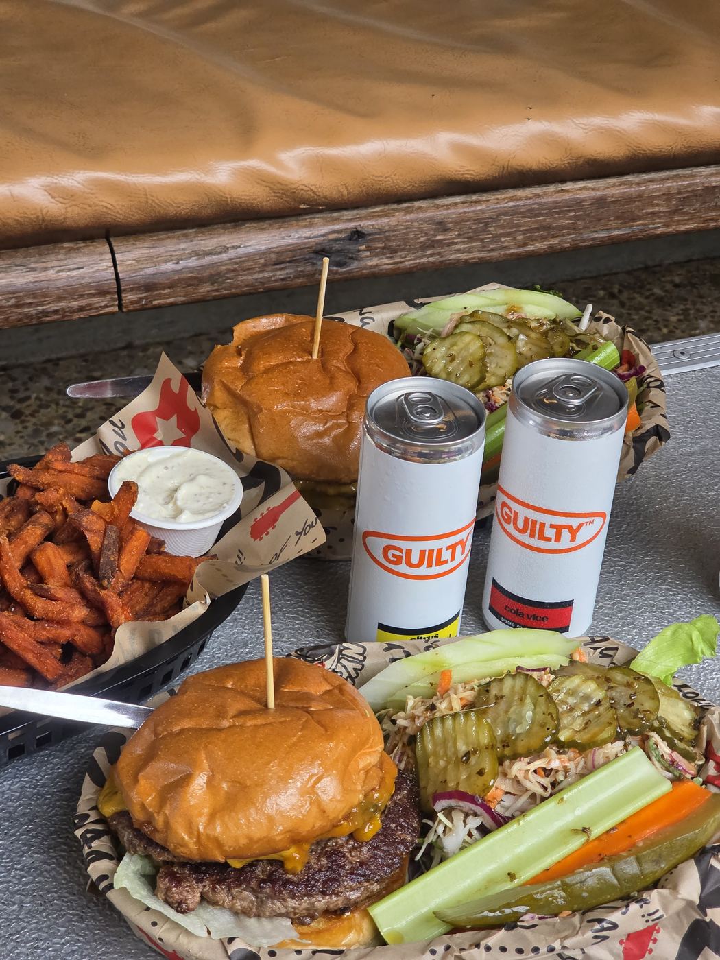 Two Guilty cans next to burgers and fries